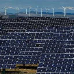 Ogromna elektrownia słoneczna w Hiszpanii, z rzędami paneli i wiatrakami w tle, symbolizuje zieloną energię.