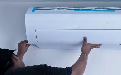Technik montuje białą jednostkę klimatyzacyjną na jasnej ścianie.