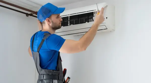 Technik w niebieskiej czapce i ogrodniczkach naprawia klimatyzator.