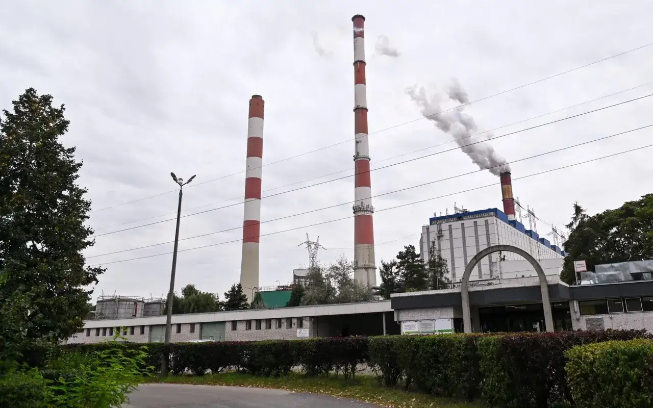 Dwa wysokie kominy z czerwonymi pasami górują nad budynkami elektrowni Dolna Odra. Z jednego z nich unosi się dym.